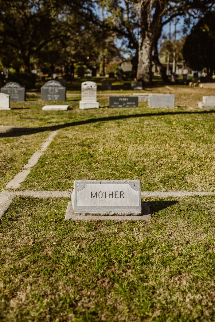 About A peaceful cemetery scene with a gravestone marked 'Mother', surrounded by greenery.