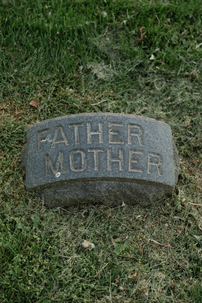 A gravestone with 'Father Mother' text on grass, symbolizing remembrance.